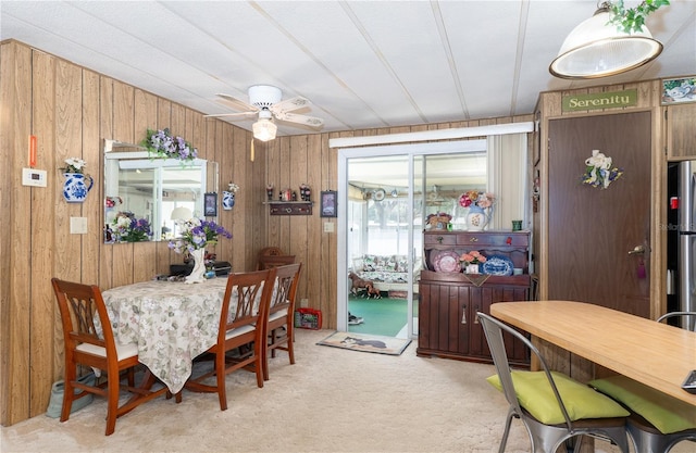 dining area featuring light carpet, ceiling fan, and wooden walls