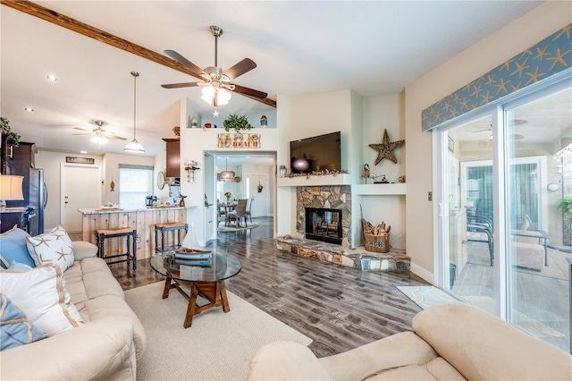 living room with a stone fireplace, wood finished floors, a ceiling fan, baseboards, and vaulted ceiling