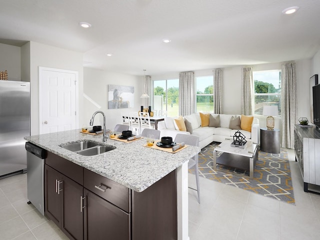 kitchen with a sink, open floor plan, dark brown cabinetry, appliances with stainless steel finishes, and light stone countertops