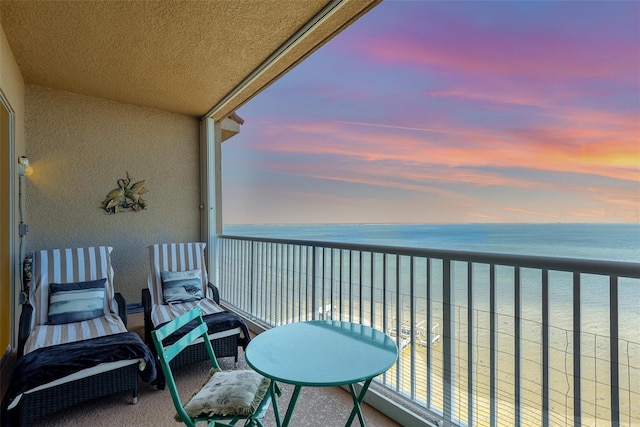 balcony at dusk featuring a water view