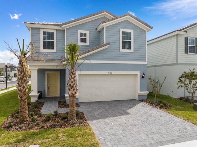 view of front of home with decorative driveway, a tile roof, an attached garage, and stucco siding