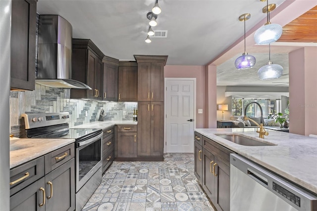 kitchen featuring a sink, decorative backsplash, stainless steel appliances, wall chimney range hood, and decorative light fixtures