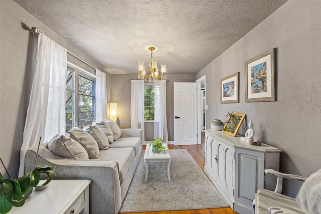 living room featuring a notable chandelier, a textured wall, light wood-type flooring, and a textured ceiling