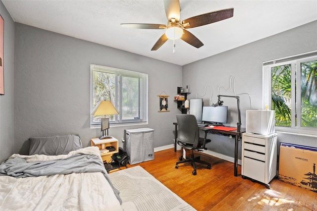 bedroom featuring baseboards, wood finished floors, a ceiling fan, and a textured wall