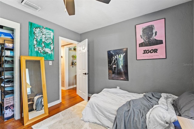 bedroom with a ceiling fan, wood finished floors, visible vents, and baseboards