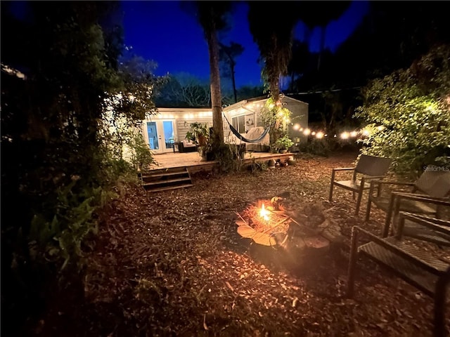 yard at night with french doors, a fire pit, and a deck