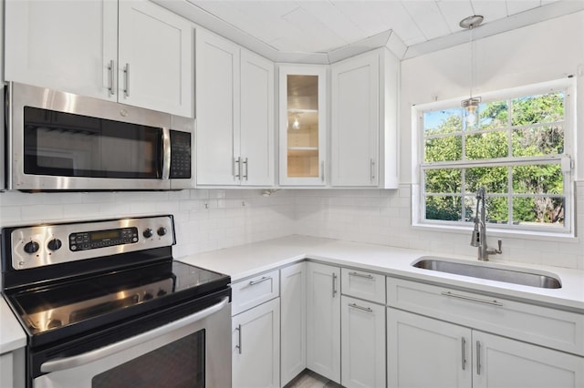 kitchen featuring white cabinets, decorative backsplash, appliances with stainless steel finishes, light countertops, and a sink