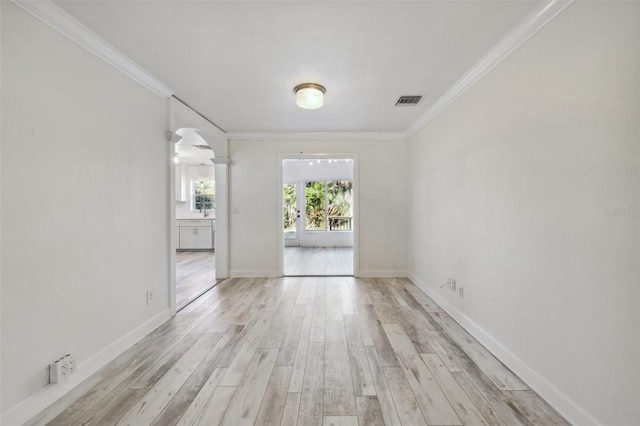 empty room featuring visible vents, arched walkways, baseboards, light wood-style flooring, and ornamental molding