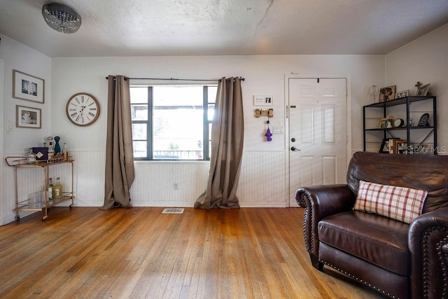 living area with a textured ceiling, light wood-style flooring, wainscoting, and visible vents