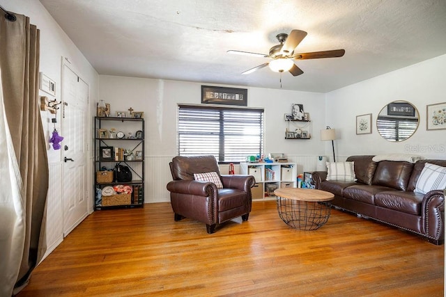 living room with a wainscoted wall, ceiling fan, and light wood finished floors