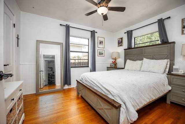 bedroom with a wainscoted wall, ceiling fan, multiple windows, and light wood-style flooring