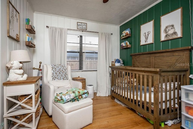 bedroom featuring a crib, light wood-style floors, and crown molding