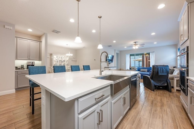 kitchen with dishwasher, light wood-style flooring, open floor plan, a kitchen breakfast bar, and light countertops