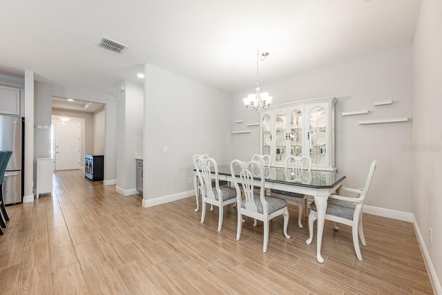 dining space with a notable chandelier, light wood-style flooring, visible vents, and baseboards