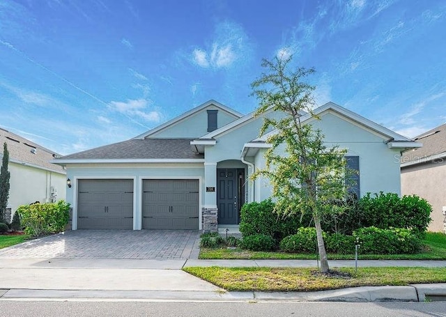 ranch-style house featuring roof with shingles, decorative driveway, an attached garage, and stucco siding