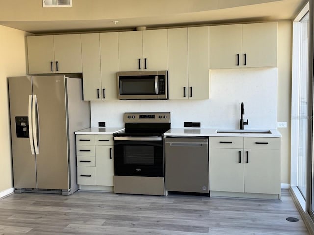 kitchen with stainless steel appliances, cream cabinets, a sink, and light countertops