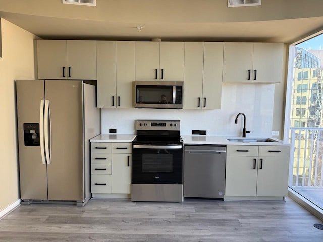 kitchen with stainless steel appliances, light countertops, visible vents, light wood-style floors, and a sink