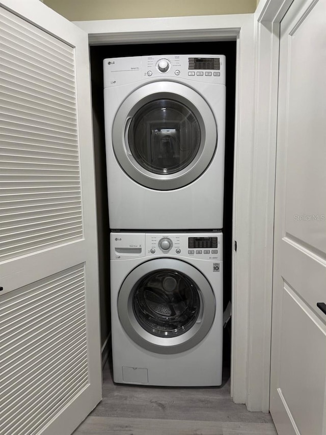 clothes washing area featuring laundry area, stacked washer / dryer, and wood finished floors