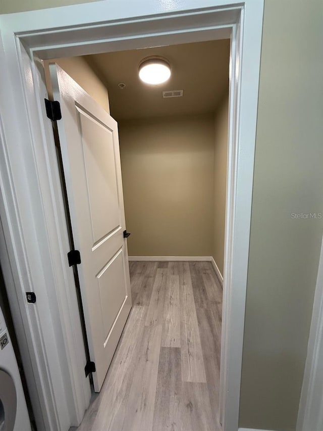 hallway with light wood finished floors, visible vents, and baseboards