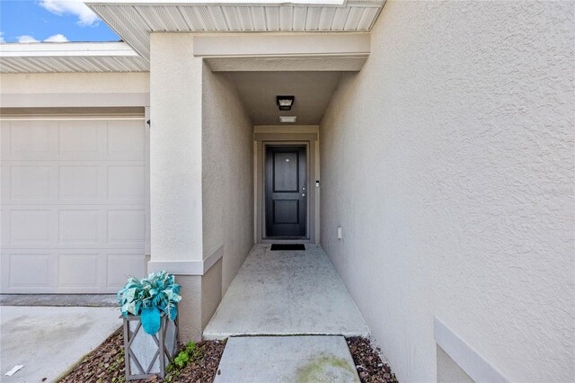 view of exterior entry with an attached garage and stucco siding