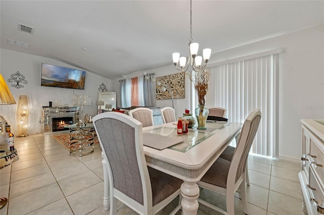 dining area with visible vents, light tile patterned flooring, vaulted ceiling, a chandelier, and a warm lit fireplace