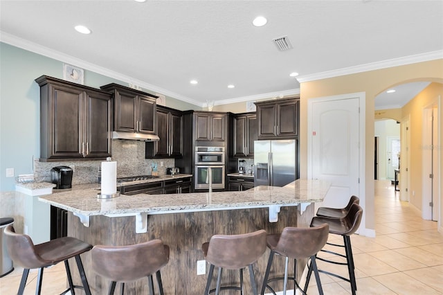 kitchen with visible vents, light tile patterned flooring, arched walkways, under cabinet range hood, and appliances with stainless steel finishes