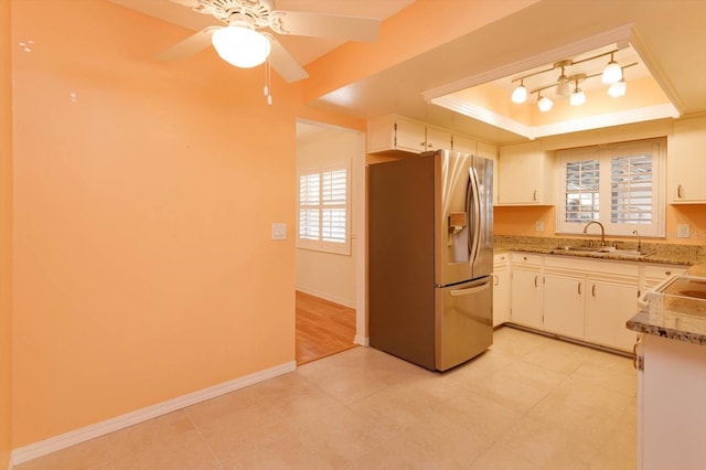 kitchen with stainless steel refrigerator with ice dispenser, a raised ceiling, white cabinets, a sink, and baseboards