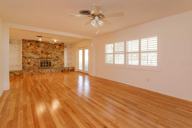 unfurnished living room with light wood finished floors, built in features, a ceiling fan, a stone fireplace, and french doors