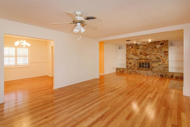 unfurnished living room with light wood-type flooring, a ceiling fan, a textured ceiling, and a stone fireplace