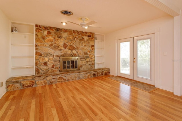 unfurnished living room with visible vents, wood finished floors, french doors, built in shelves, and a fireplace