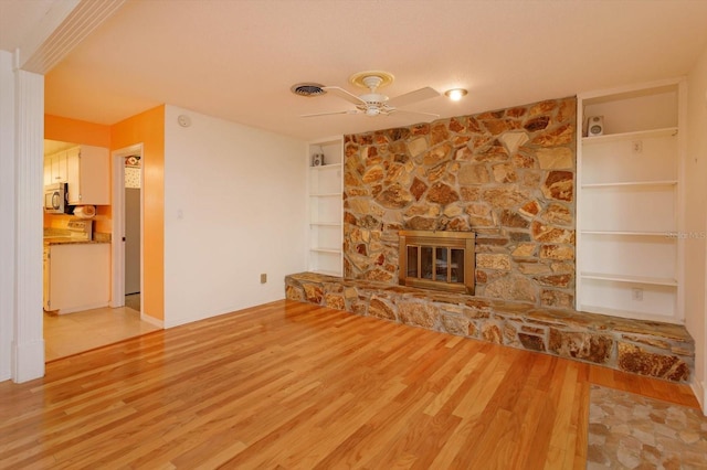 unfurnished living room with built in features, visible vents, a ceiling fan, wood finished floors, and a fireplace