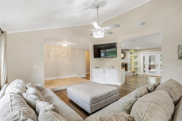 living area with a fireplace with raised hearth, wood finished floors, visible vents, baseboards, and crown molding