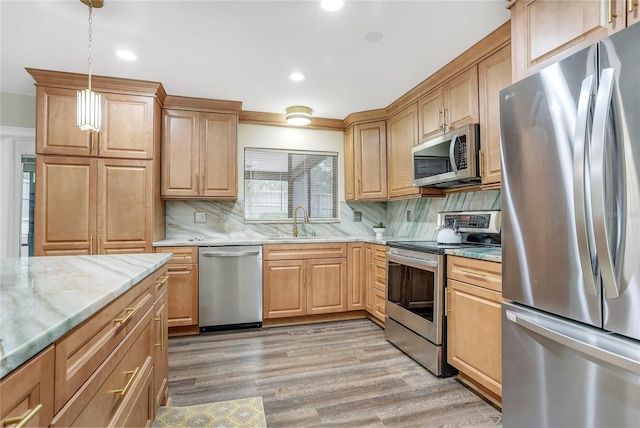 kitchen with tasteful backsplash, appliances with stainless steel finishes, light stone countertops, light wood-style floors, and a sink