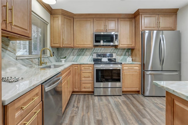 kitchen with light stone counters, stainless steel appliances, a sink, light wood-style floors, and tasteful backsplash