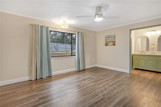 interior space with ensuite bathroom, a sink, wood finished floors, baseboards, and crown molding