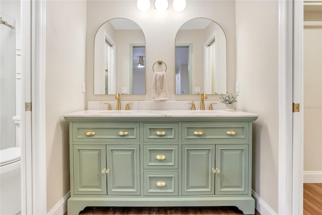 full bath featuring double vanity, baseboards, toilet, and a sink