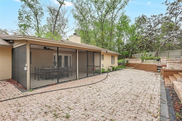 rear view of house featuring a chimney, stucco siding, a sunroom, a patio area, and fence