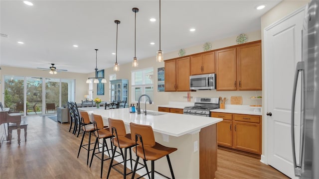 kitchen featuring light wood finished floors, a sink, appliances with stainless steel finishes, a ceiling fan, and a kitchen island with sink