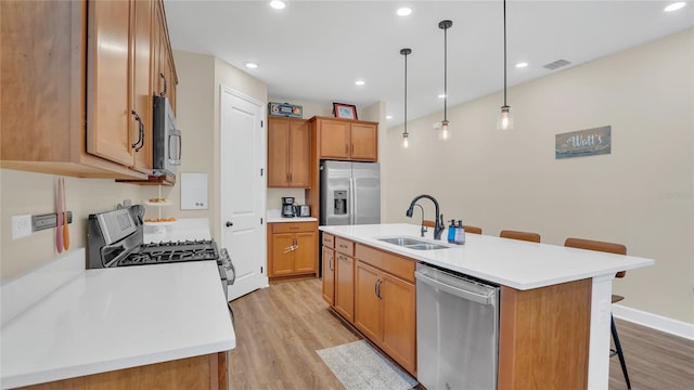 kitchen with visible vents, a kitchen bar, light wood-style flooring, stainless steel appliances, and a sink