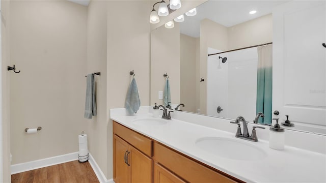 full bath with a shower with curtain, a sink, wood finished floors, double vanity, and baseboards
