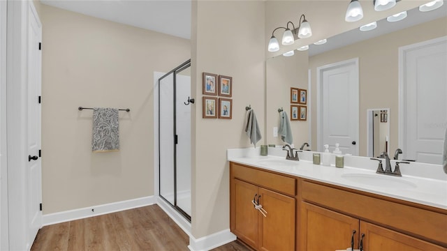 bathroom featuring double vanity, a stall shower, wood finished floors, and a sink