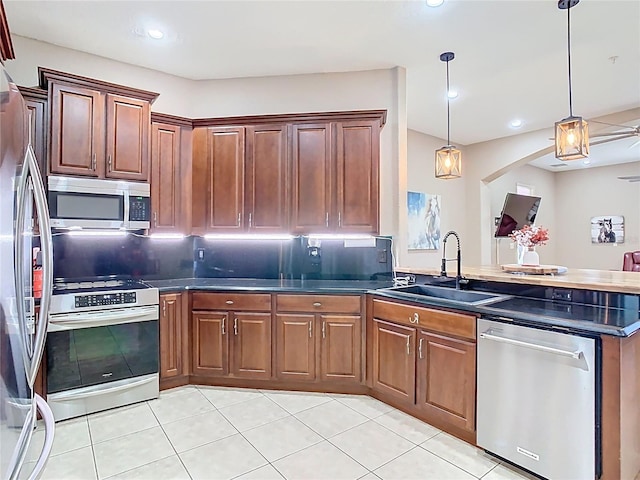 kitchen with a peninsula, a sink, stainless steel appliances, dark countertops, and decorative light fixtures