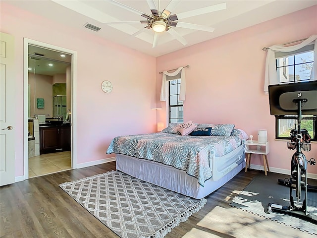 bedroom with ensuite bath, wood finished floors, visible vents, and baseboards