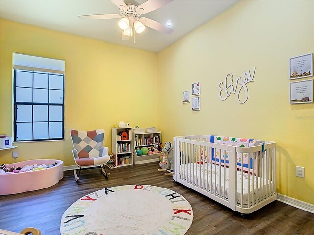 bedroom with baseboards, a crib, wood finished floors, and a ceiling fan