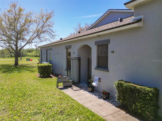 property entrance featuring a shingled roof, a yard, and stucco siding