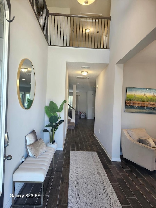 hallway featuring visible vents, stairway, a high ceiling, wood tiled floor, and baseboards