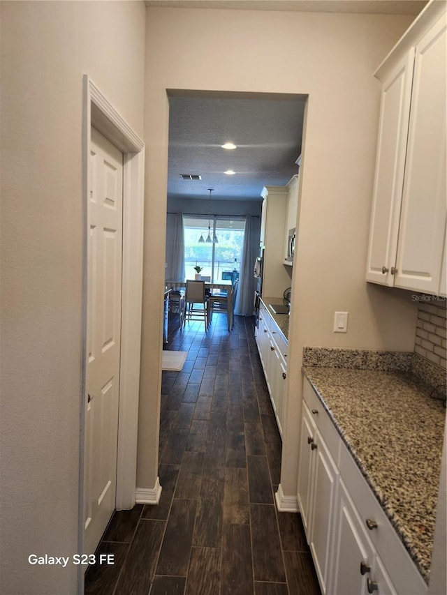 hallway featuring baseboards, visible vents, and wood finish floors