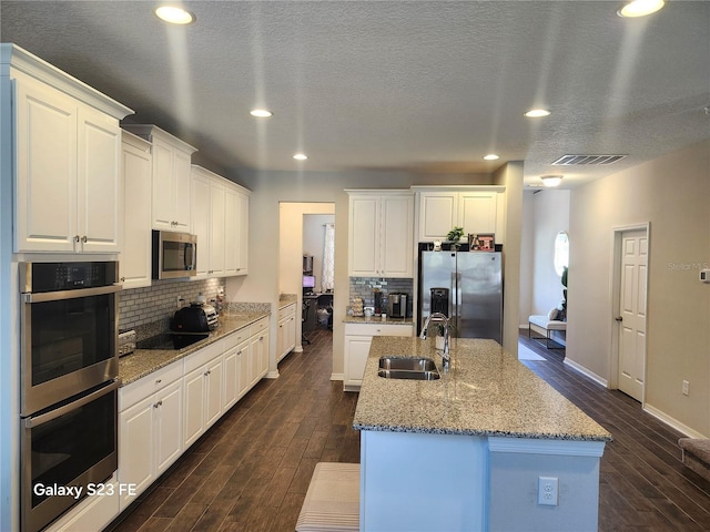 kitchen with visible vents, dark wood-style flooring, a kitchen island with sink, stainless steel appliances, and a sink