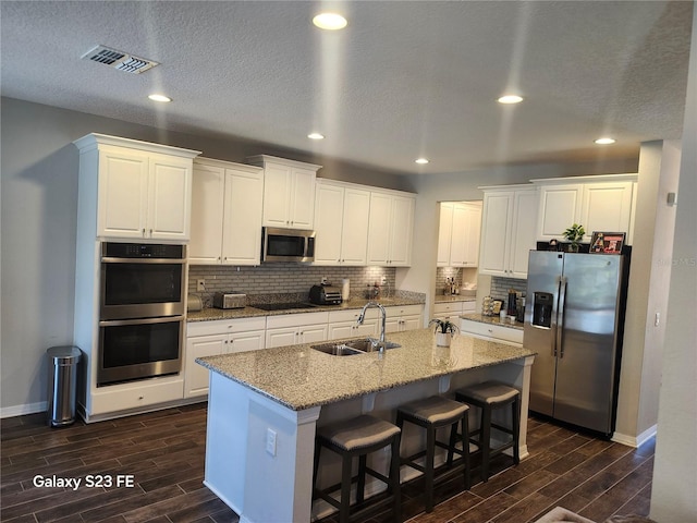 kitchen featuring wood finish floors, a sink, visible vents, appliances with stainless steel finishes, and tasteful backsplash