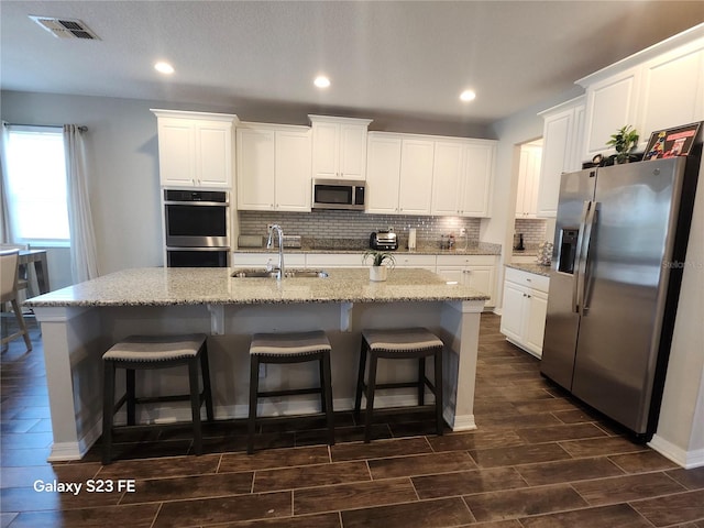 kitchen featuring wood finish floors, visible vents, appliances with stainless steel finishes, white cabinets, and a sink